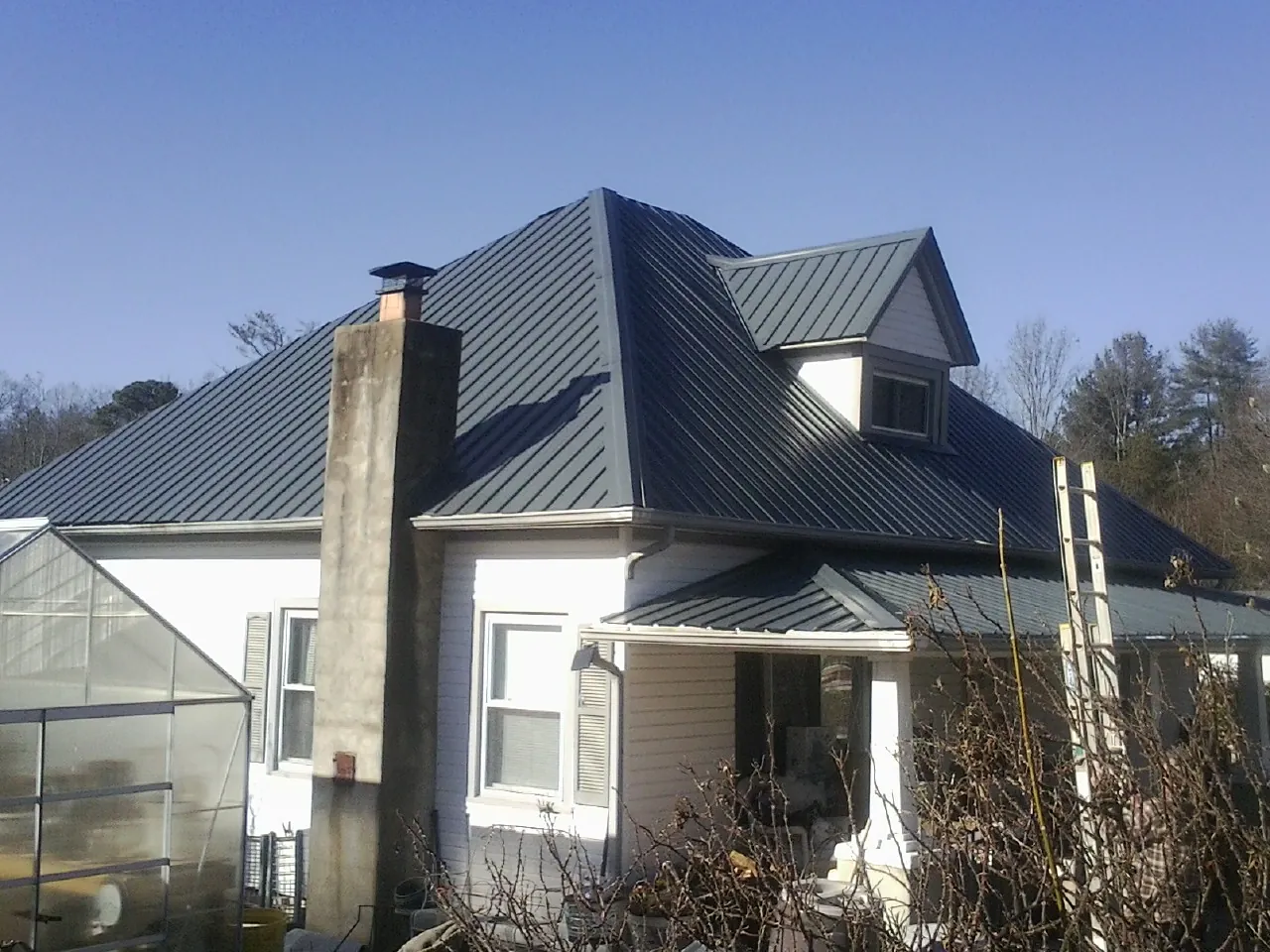 Dark blue standing seam metal roof on a white farmhouse with dormer — Slate & Tile Roof Repair by Roofing Brothers in Parksley