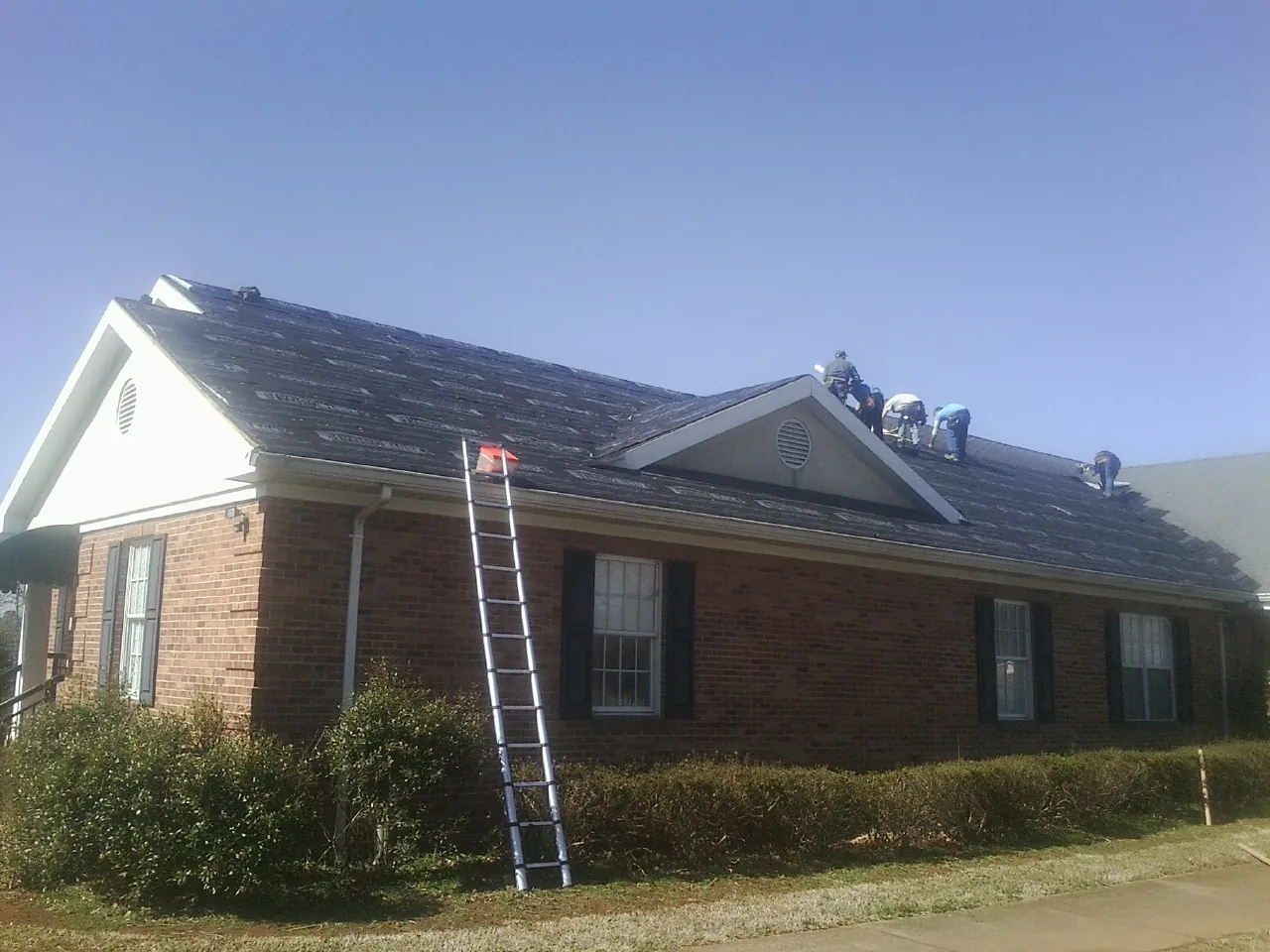 Crew tearing shingles off a brick ranch roof with a ladder set — Metal Roof Repair work by our crew in Parksley