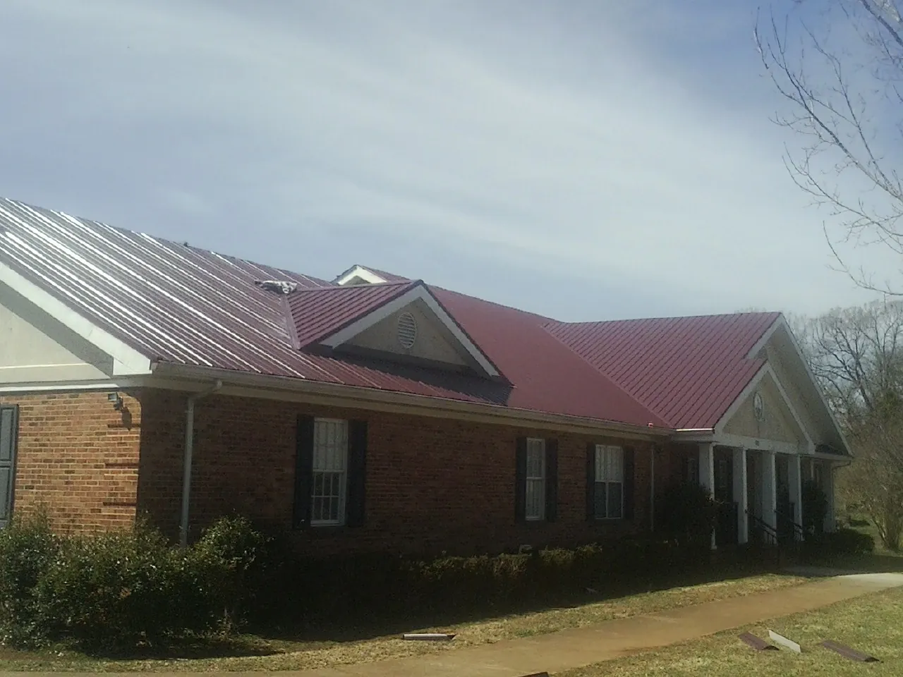 Red metal roof with gabled entries on a long brick building, from a Hail Damage Roof Repair job in Parksley