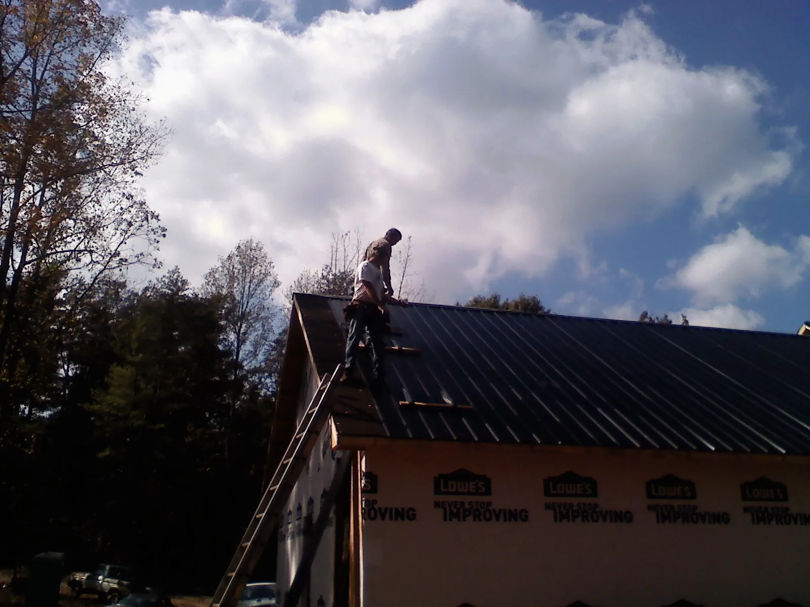 Roofer fastening dark metal panels high against a cloudy sky, from a Roof Inspection job in Parksley