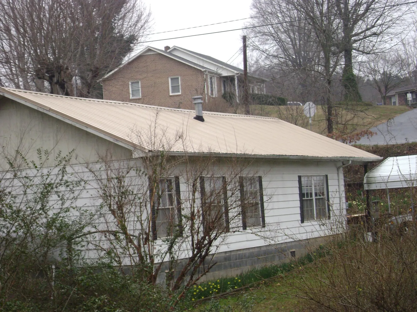Tan metal roof on a white sided house set into a hillside — Commercial Roofing by Roofing Brothers in Parksley