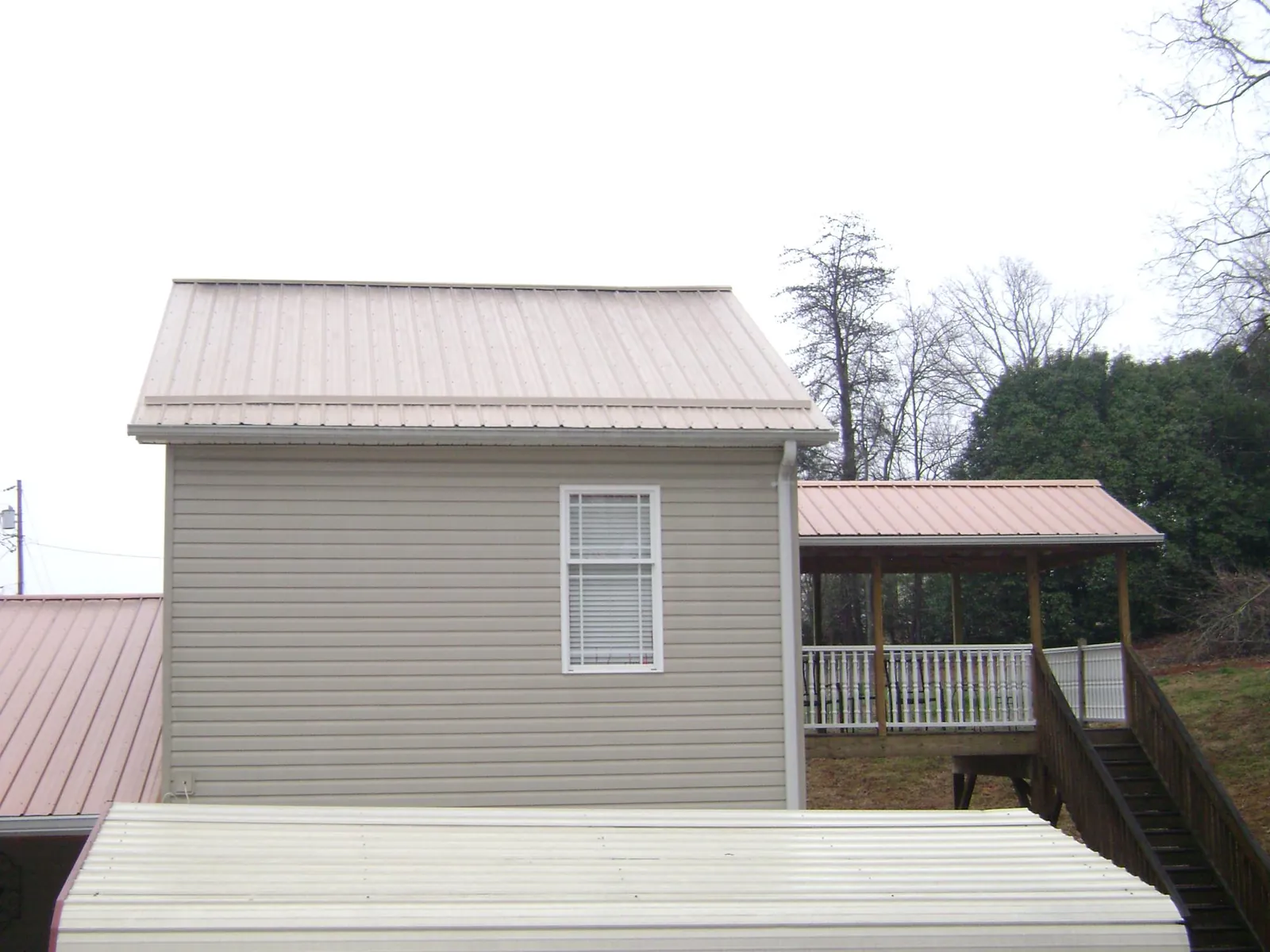 Tan metal roofs on a two story addition and attached porch, from a Roof Replacement job in Parksley